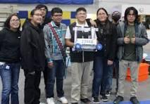 Group of six students with a robot at a robotics competition in a gymnasium, smiling and posing for the camera.