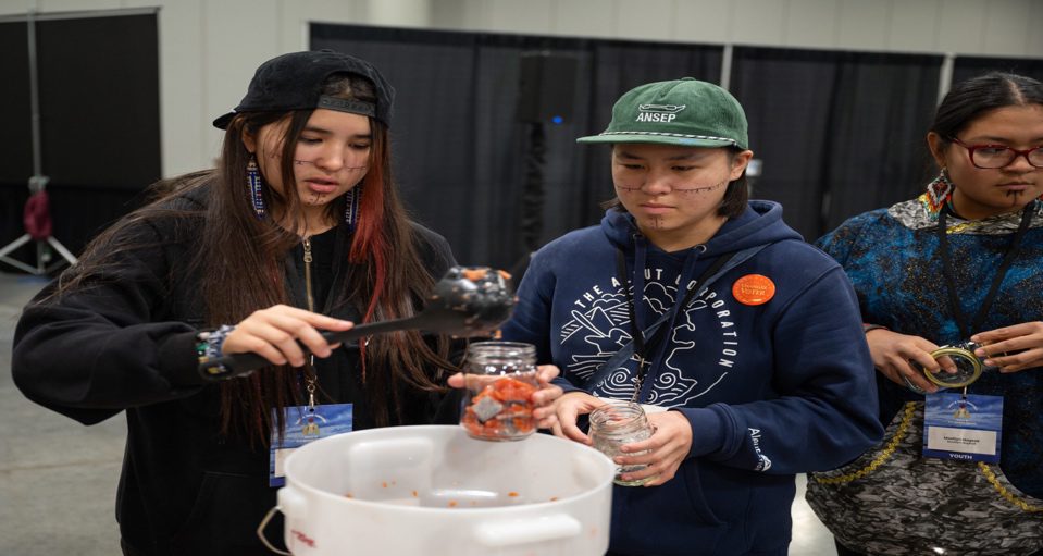 Two young adults engaged in a scientific activity, transferring a liquid between containers at a conference.