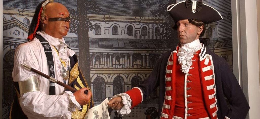 Two men in historical costumes, one as a pirate and the other in a british redcoat uniform, shaking hands in front of a vintage architectural illustration.